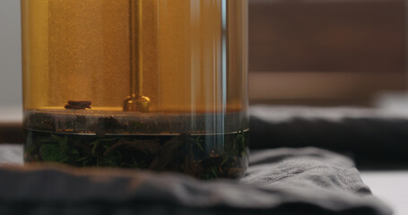 pressing plunge black tea with thyme and mint in beaker glass closeup