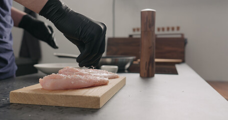 man hands add salt flakes on chicken fillet on oak board