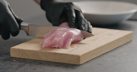 man hands in black gloves slicing turkey fillet on oak wood board