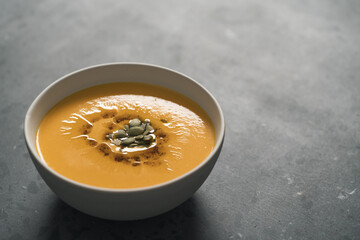 Pumpkin soup decorated with pumpkin seeds oil in white bowl on concrete background with copy space