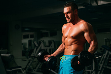 Fototapeta na wymiar Sport man man doing biceps lifting in a gym. Young muscular man with naked torso working out in gym. Athletic male sport man exercising. Fitness sports concept.