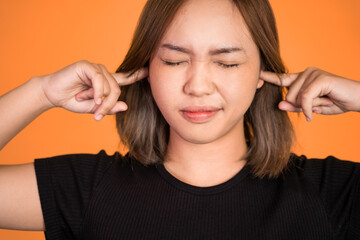 asian woman with annoyed expression covering ears with both hands on isolated background