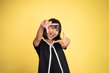 Obraz premium young woman looking at the camera from between fingers forming a frame on isolated background