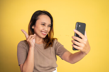 attractive woman take a selfie using mobile phone camera with v sign finger gesture on isolated background