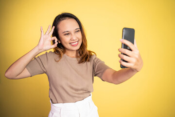 smiling asian woman take a selfie with ok hands gesture on isolated background