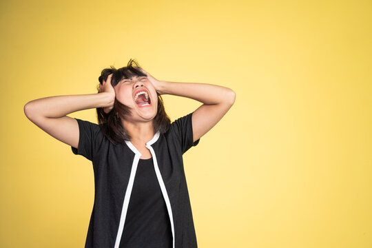 frustrated Asian young woman holding head with headache on isolated orange background
