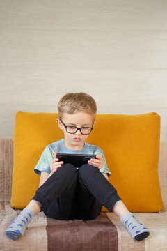 A boy of five years old, of European appearance, uses the phone.A boy of five years old, of European appearance, sits on the sofa and uses the phone