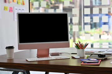 Close-up front view of a blank computer monitor screen with any gadgets and accessories on the wooden desk over a blurred modern office as a background. Business and Technology.