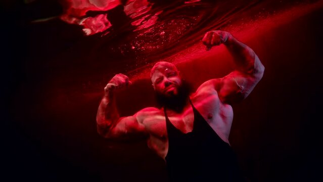 a huge bald man with a beard poses in the dark water. red light. the average plan. the camera is tilted