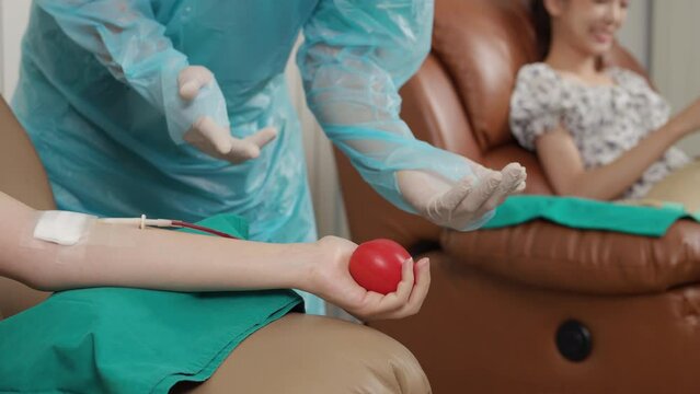 Close up of Healthcare worker in protective workwear, CPE Gown suggests the blood donor squeeze the ball for blood to come out easily. Blood Donation and charity concept. Slow Motion