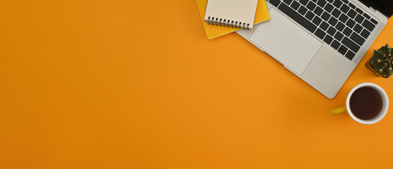 Top view position of yellow background with a laptop keyboard, a cup of coffee, notebooks, and a...