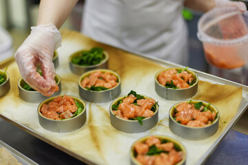 Cook is filling group of tarts with salmon at restaurant kitchen background. Culinary process