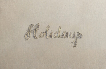 “Holidays” handwritten on sand at the beach on a warm summer day
