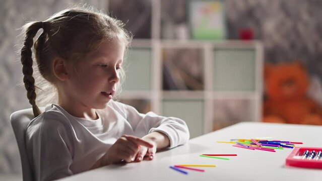 Pretty little schoolgirl with braids counts moving lips aloud plastic sticks solving problem at mental arithmetic lesson at home closeup slow motion