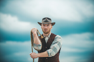 Sexy western man with cowboy hat. Cowboy with lasso rope on sky background.