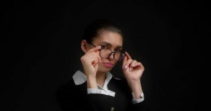 Business woman in perplexity lowers her glasses and looks at the camera with a dissatisfied expression on her face. Serious Asian woman is not satisfied with the answer. Isolated on a black background