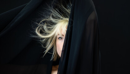 half hidden portrait of blonde sexy woman fashion model, behind black cloth, whose hair is...