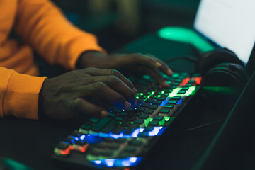 African-American man using backlit colorful keyboard in dark room closeup . High quality photo