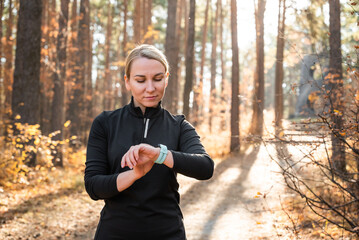 Active girl with fitness tracker smart watch running in the autumn park outdoors, viewing health data while doing sports by touching the screen of her smart watch