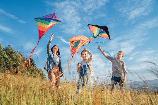 Smiling gils and brother boy running with flying colorful kites on the high grass meadow in the mountain fields. Happy childhood moments or outdoor time spending concept image.