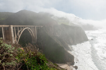 Bixby Canyon Bridge during a beautiful sunny afternoon, while a thin fog is creeping up from the sea.