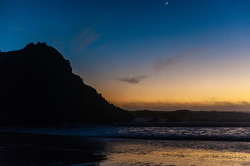 Fototapeta na wymiar Bright orange sky at Pfeiffer beach, around sunset. Small crescent moon is in the background.