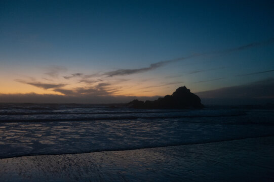 Rocks in the surf of Pfeiffer beach, around sunset. Deep yellow orange clouds color the sky.