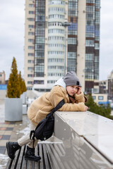 a cute seven-year-old girl in a faux fur coat stands near the parapet in the city