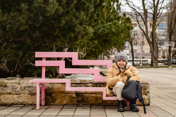 a cute six-year-old girl in a beige fur coat made of eco-friendly faux fur is sitting on a bench