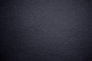 Photo of a black color texture. Black background for the text made of soft felt fabric. Dark textured background with vignette around the edges.