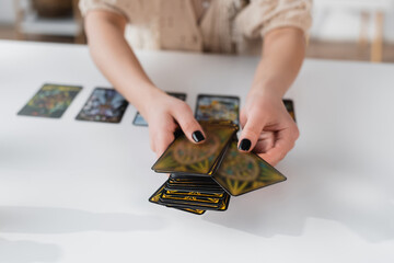 Cropped view of medium holding blurred tarot cards near table.