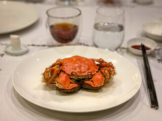 One cooked Chinese style seasonal hairy crab on a white plate with glasses of drinks on the background