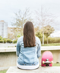 Girl sitting with her back turned and a skateboard at her side