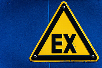 czarno żółty znak na niebieskiej ścianie z literami EX