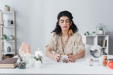 Gypsy soothsayer touching magic crystals near book, orb and candles on table.