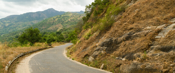 Empty narrow road in hilly tropical landscape with cloudy skies