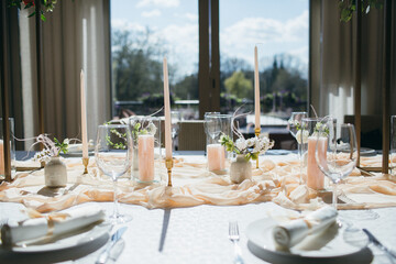 banquet tables with white tablecloths are in the hall of the old house, on the tables are flower arrangements, candles, plates with napkins, glasses and cutlery