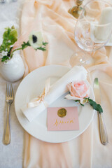 banquet tables with white tablecloths are in the hall of the old house, on the tables are flower arrangements, candles, plates with napkins, glasses and cutlery