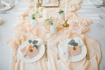banquet tables with white tablecloths are in the hall of the old house, on the tables are flower arrangements, candles, plates with napkins, glasses and cutlery