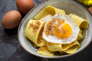 Close-up of parmesan broth with rag pasta and crispy fried egg in a grey bowl, horizontal shot, selective focus