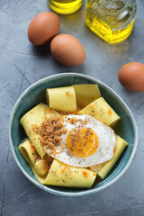 Bowl of italian rag pasta with crispy fried egg in parmesan broth, elevated view on a grey concrete background, vertical shot
