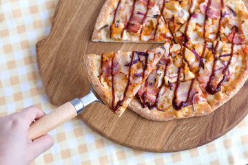 woman's hand takes a slice of pizza with a spatula with a wooden handle