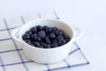 Blue garden berry. Large garden blueberries in a white plate on a blue checkered napkin. Food photography, side view