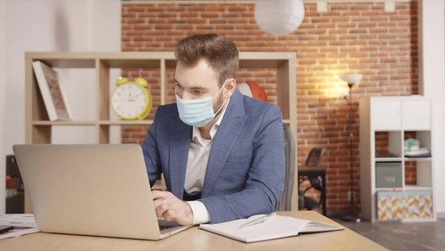A young man in a mask in the office types something on a laptop, then freaks out, takes off his mask and throws it aside. Slow motion 4k footage