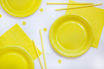 Yellow paper disposable plates, napkins and straws for drinks on white background. Table setting for picnic. Bright eco-court. Birthday, party and holiday concept. Top view, flat lay.