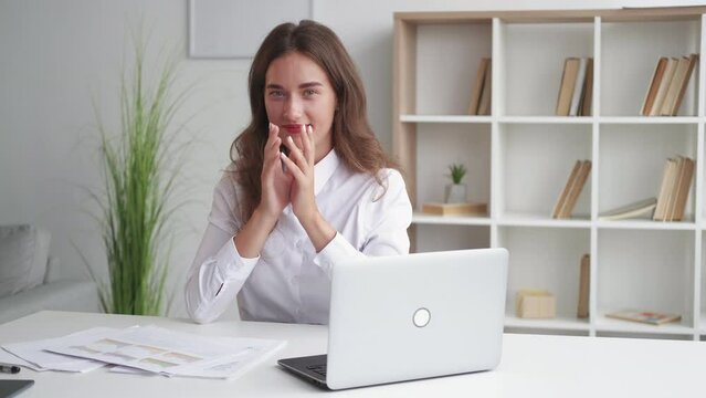 Evil plan. Office woman. Ironic expression. Pretty smiling lady in white shirt running fingers in malicious joy sitting work desk light room interior.