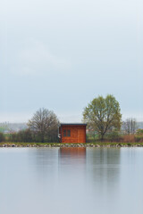 Wooden cabin, building on pond shore in rain moody weather. Long exposure, Czech landscape