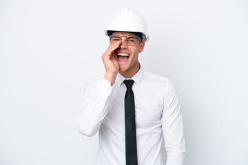 Young architect caucasian man with helmet and holding blueprints isolated on white background shouting with mouth wide open