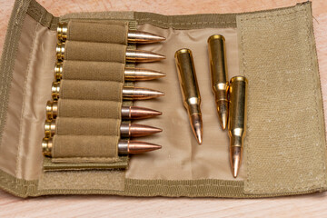Military bandolier with live ammunition from a 7.62 caliber rifle on a wooden background. - obrazy, fototapety, plakaty