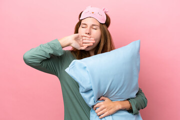 Young English woman in pajamas isolated on pink background in pajamas and holding a pillow and...